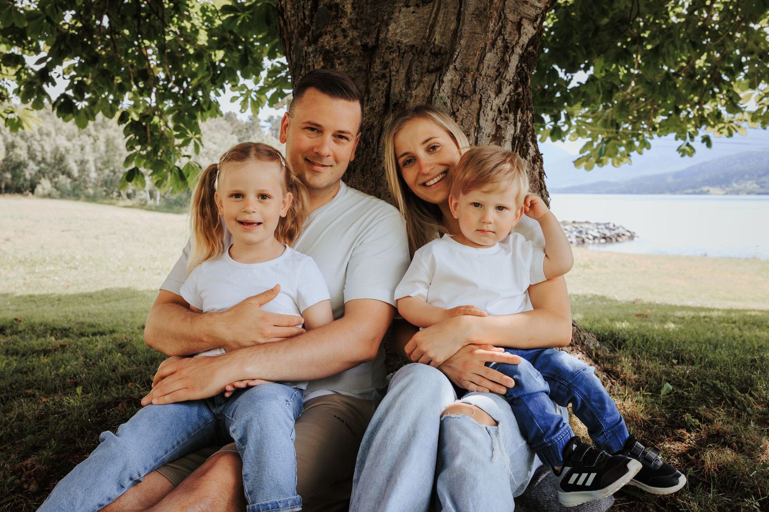 A casual family portrait taken outdoors with a lake and mountains in the background.