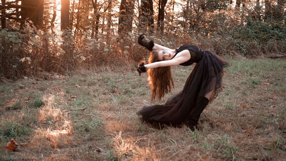 Artistic photo of a dancer in black dress bending backwards in a forest at sunset.
