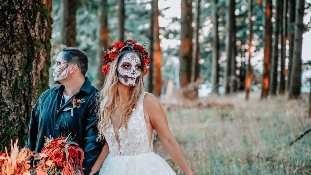 Wedding couple wearing sugar skull makeup and formal attire in a pine forest.