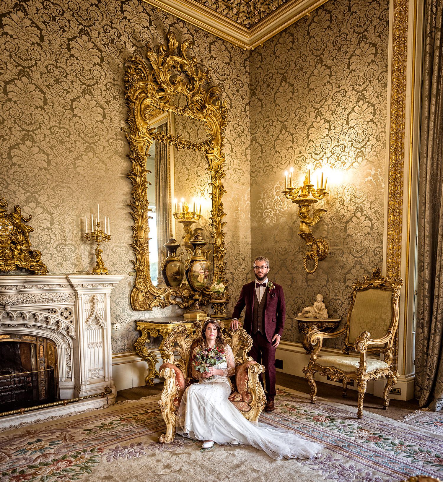 Opulent Victorian room with ornate gold mirrors, damask wallpaper and crystal wall sconces.