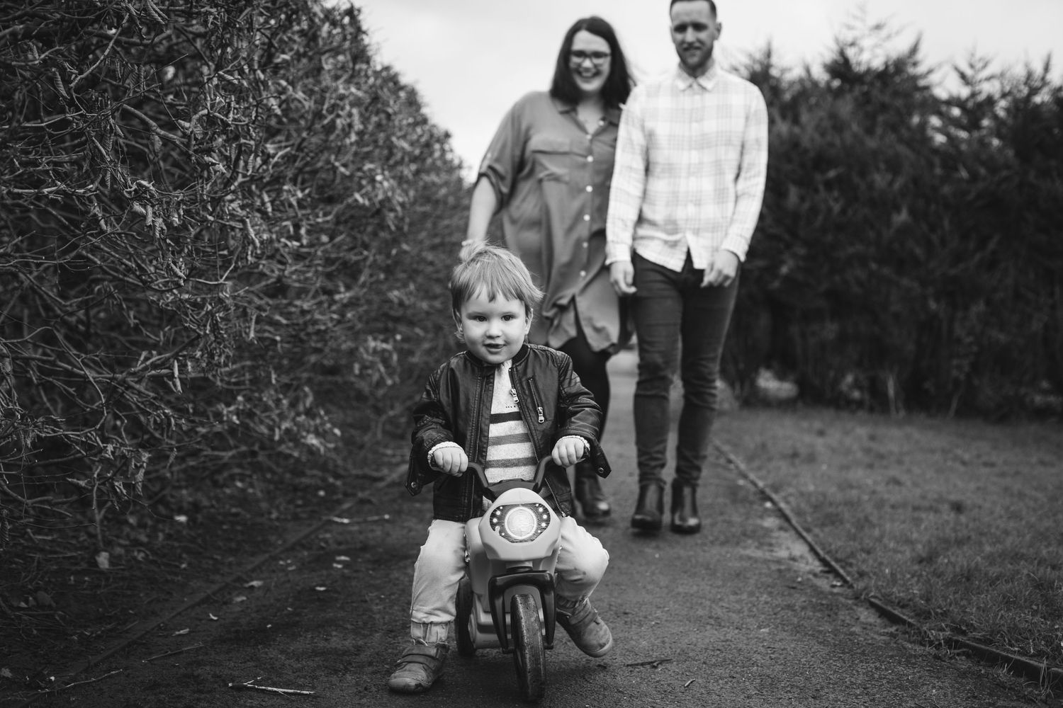 Black and white photo of a child riding a toy bike on a garden path.