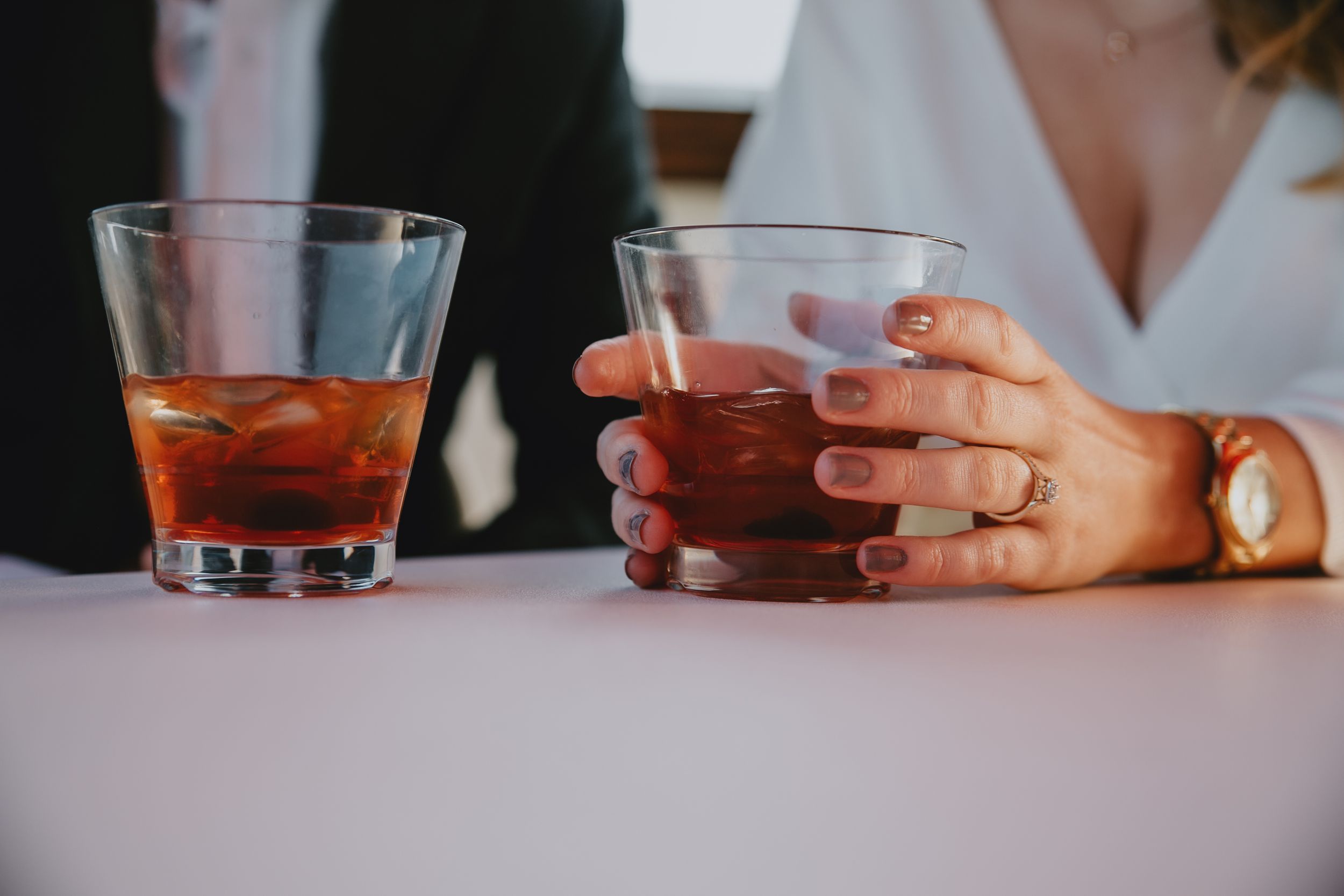 Two drinks on a table with a woman wearing a ring holding one of them
