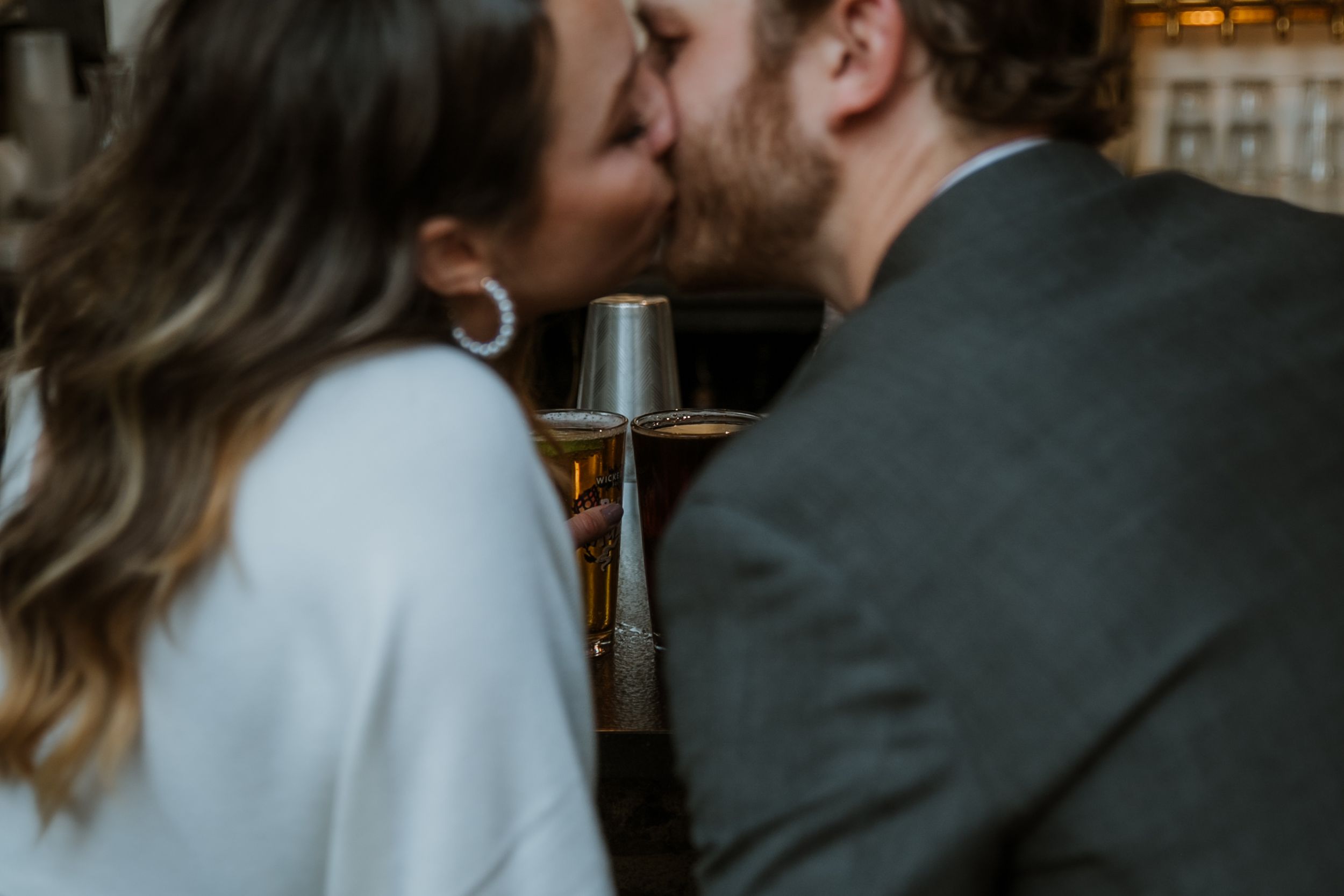 A couple shares a kiss with their drinks in focus behind them