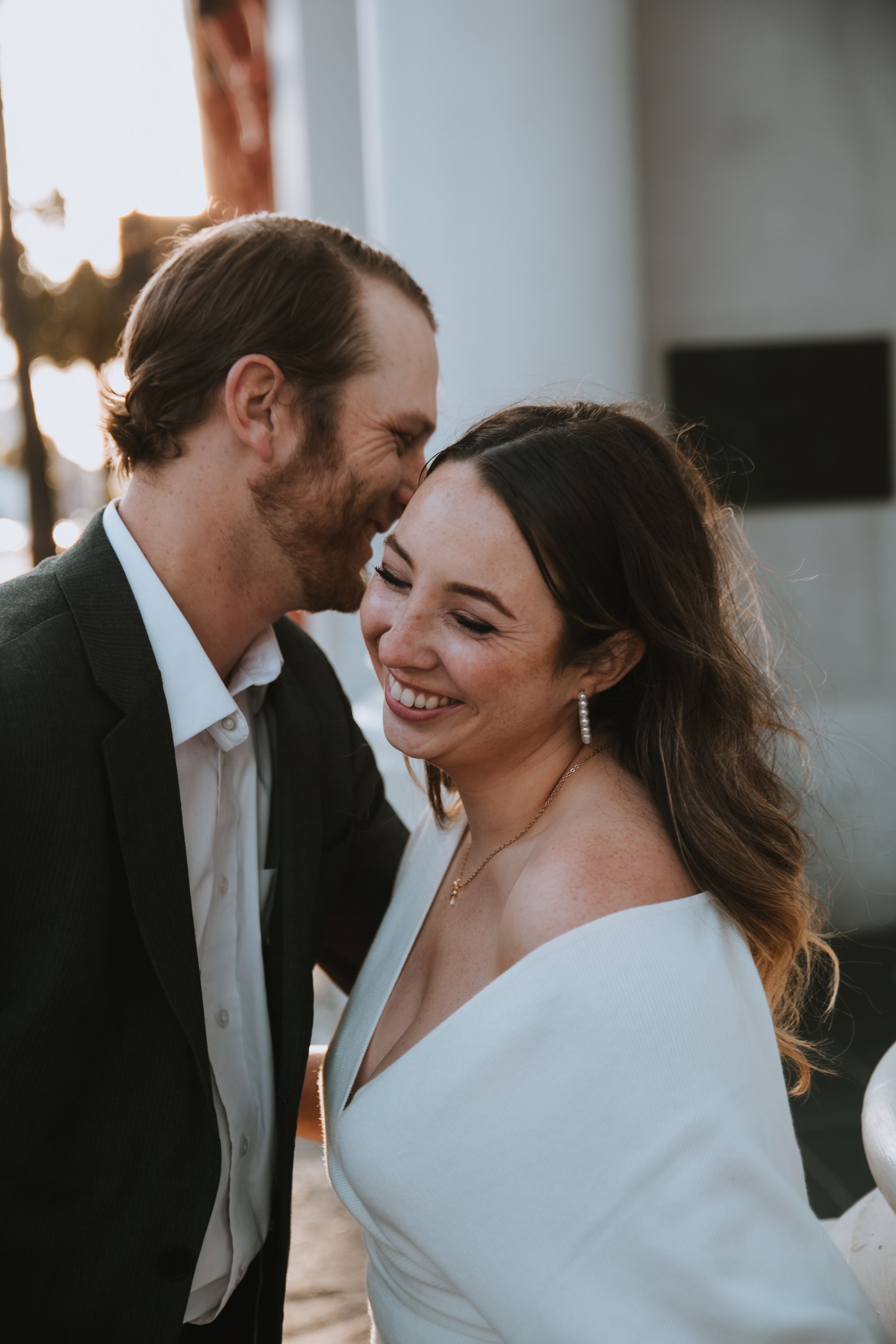 A woman laughing while her fiancé says something in her ear
