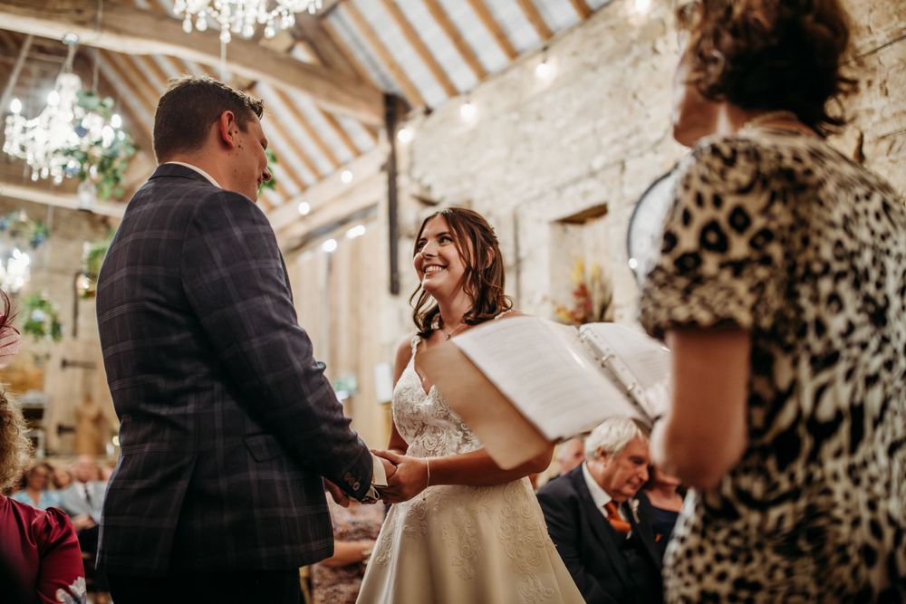 Wedding ceremony in progress inside a rustic stone barn with elegant chandeliers.