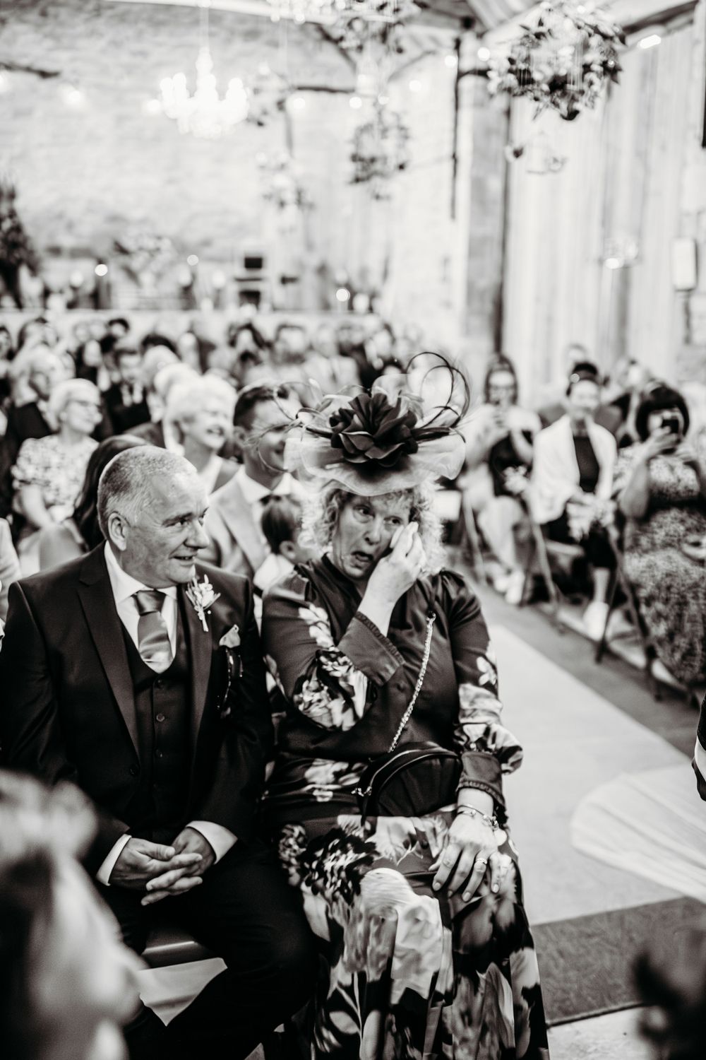 Wedding guests in formal attire watching ceremony proceedings in an elegant venue.