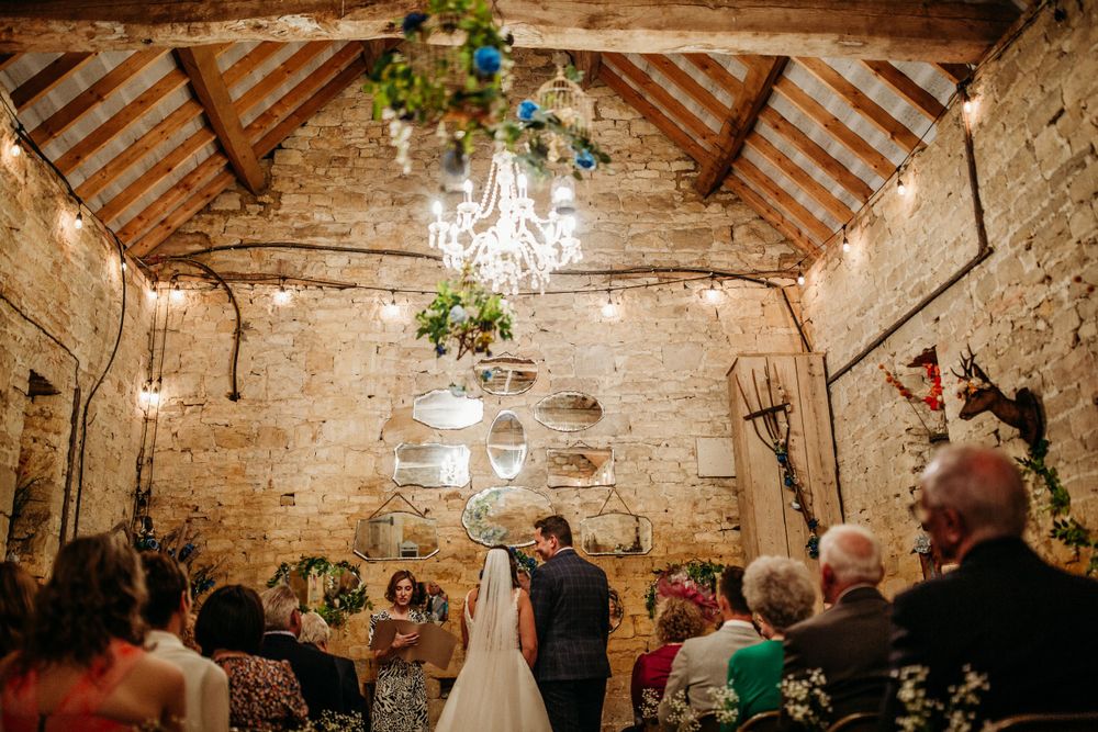 Wedding celebration in rustic barn venue with stone walls, exposed beams, and elegant chandeliers.