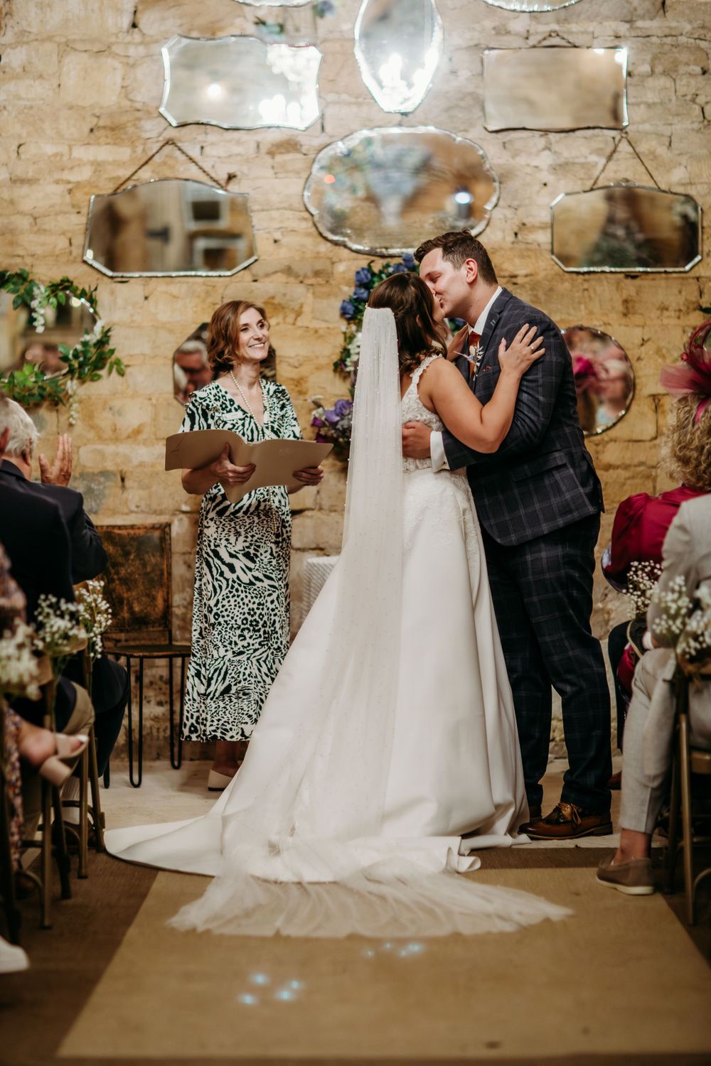 A wedding ceremony in a rustic stone venue decorated with vintage mirrors and floral arrangements.