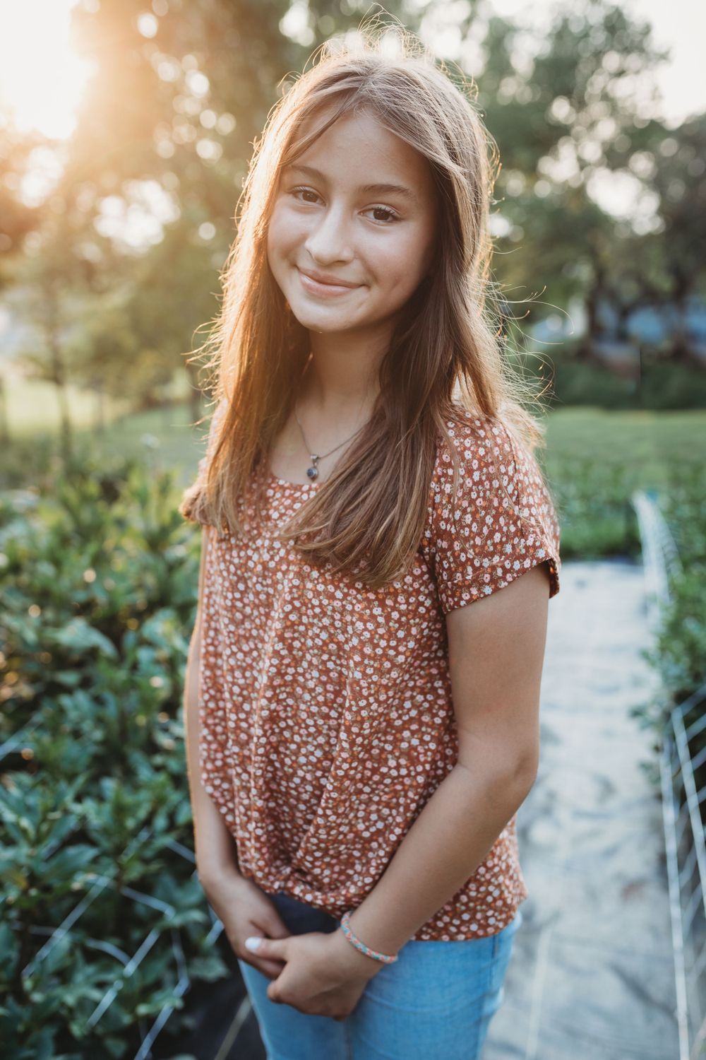 Portrait in floral peach top against garden background with evening sunlight.