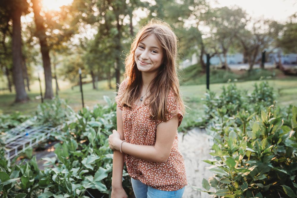 Joyful garden portrait with peach floral top and natural evening lighting.