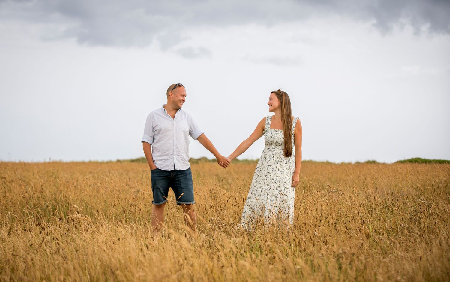 Couple walking hand in hand through tall grass field at sunset.