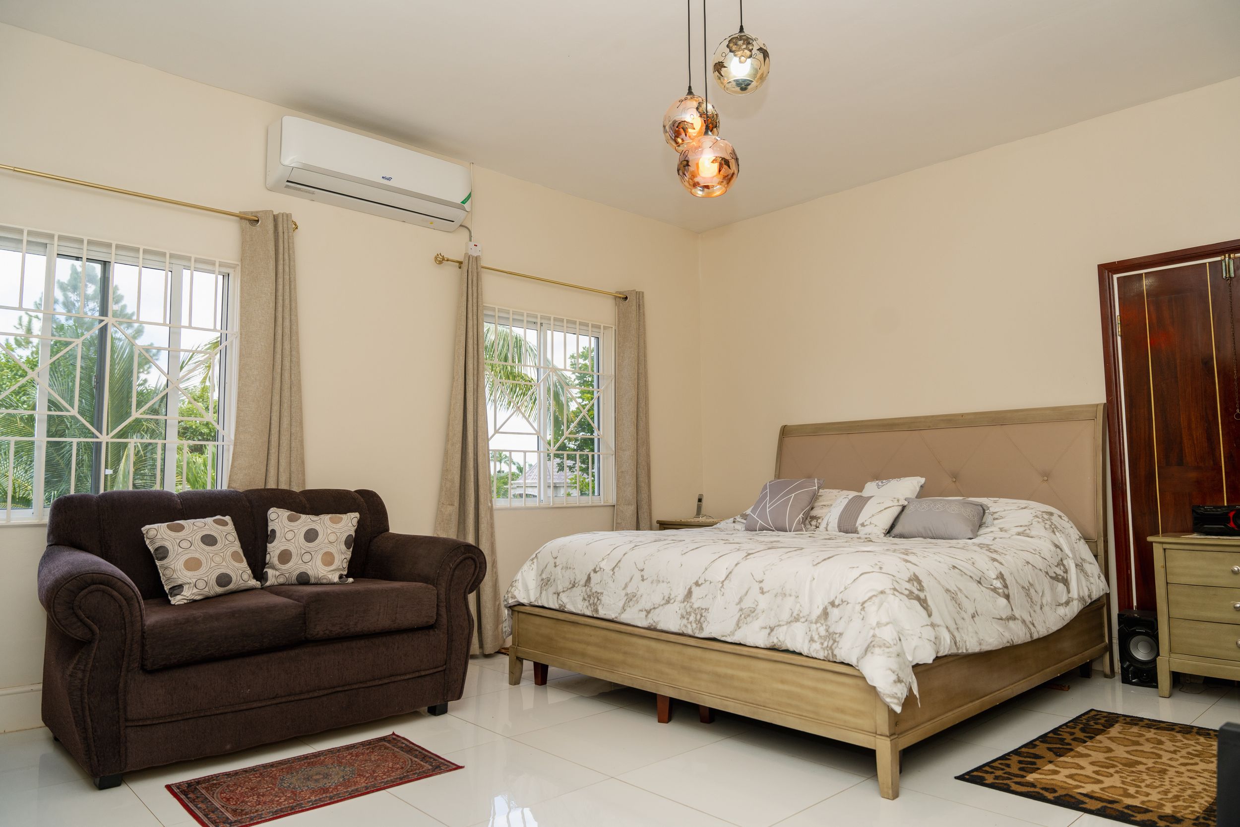 Spacious bedroom with brown sofa, large bed, and air conditioning unit installed.