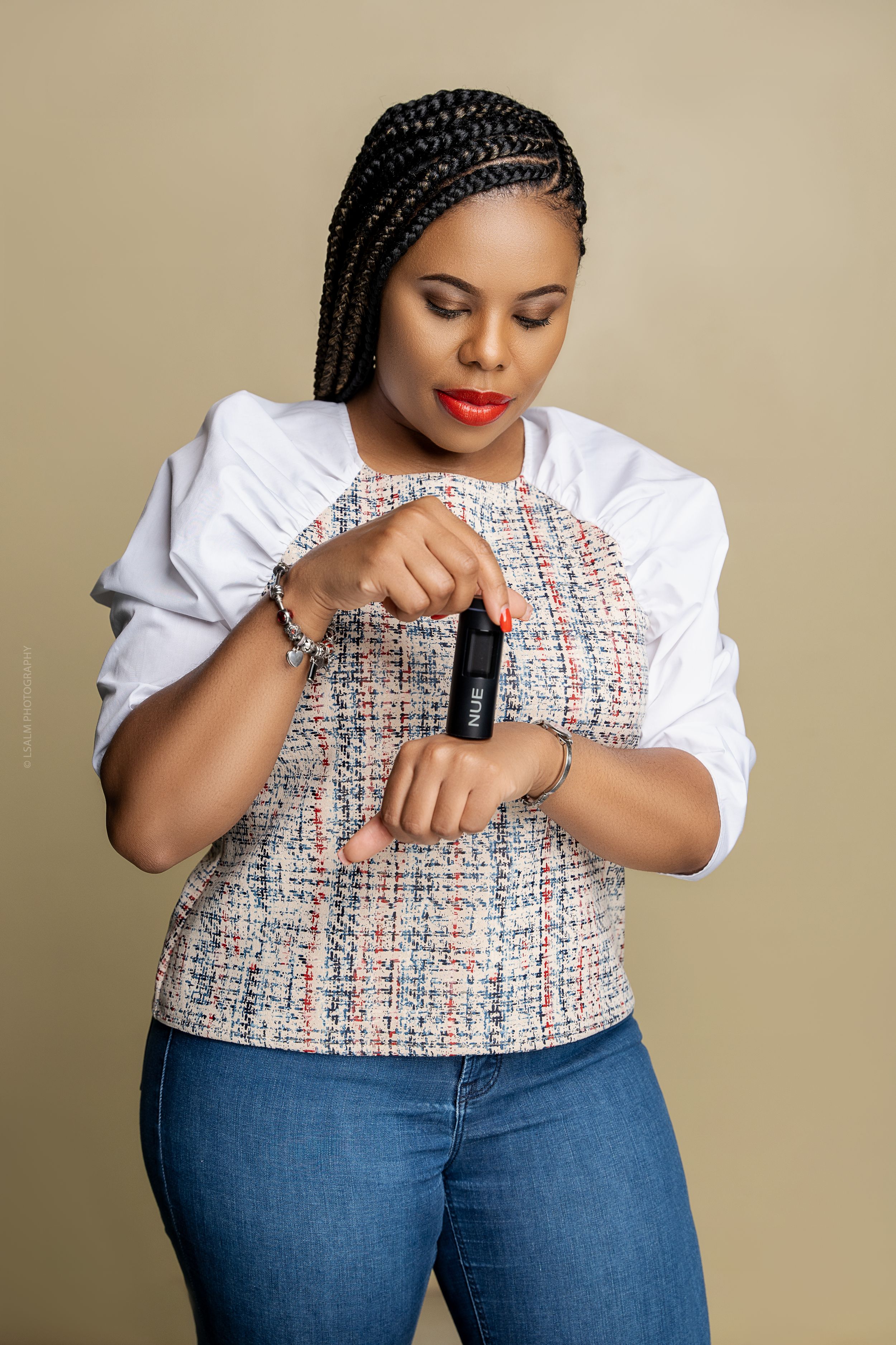 Person wearing white blouse and tweed vest checks smartwatch against beige background.
