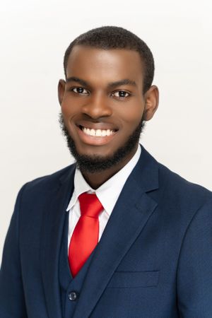 Professional headshot of someone in a navy suit and red tie against a white background.