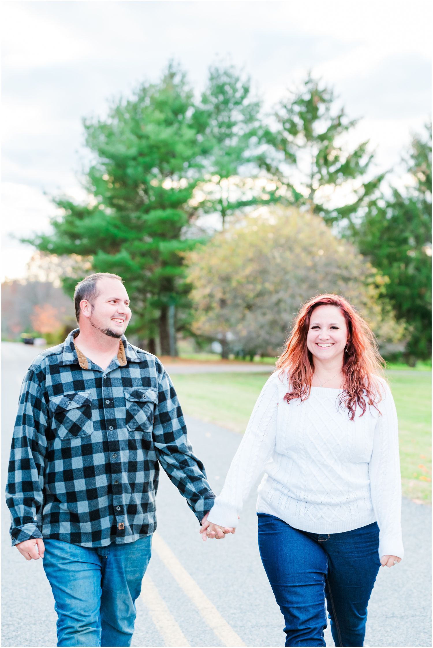 Couple walking hand in hand on a path with evergreen trees in the background.