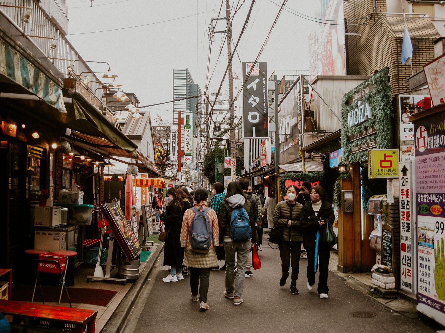 a busy Tokyo street with people walking away from the camera and buildings covered in signs surrounding them