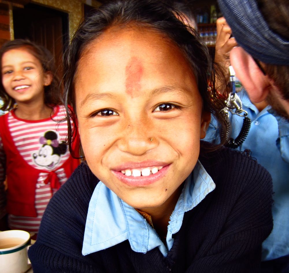 A Nepali child smiles for the camera as her friend smiles from behind her