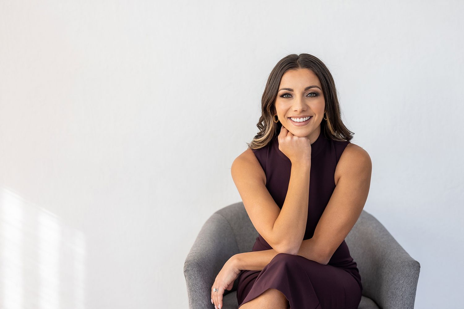 Confident woman wearing a burgundy dress sitting in a gray chair