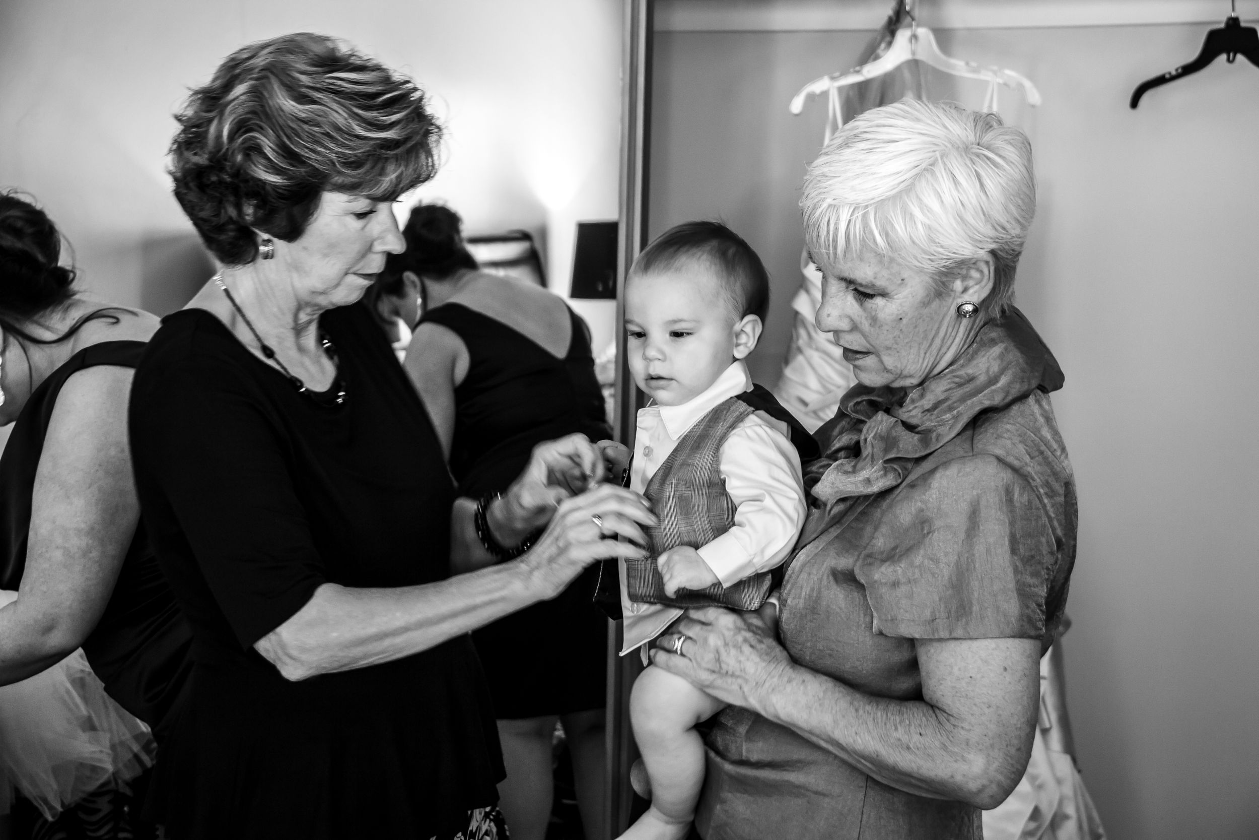 A vintage black and white photograph shows two women holding a baby in what appears to be a domestic setting.