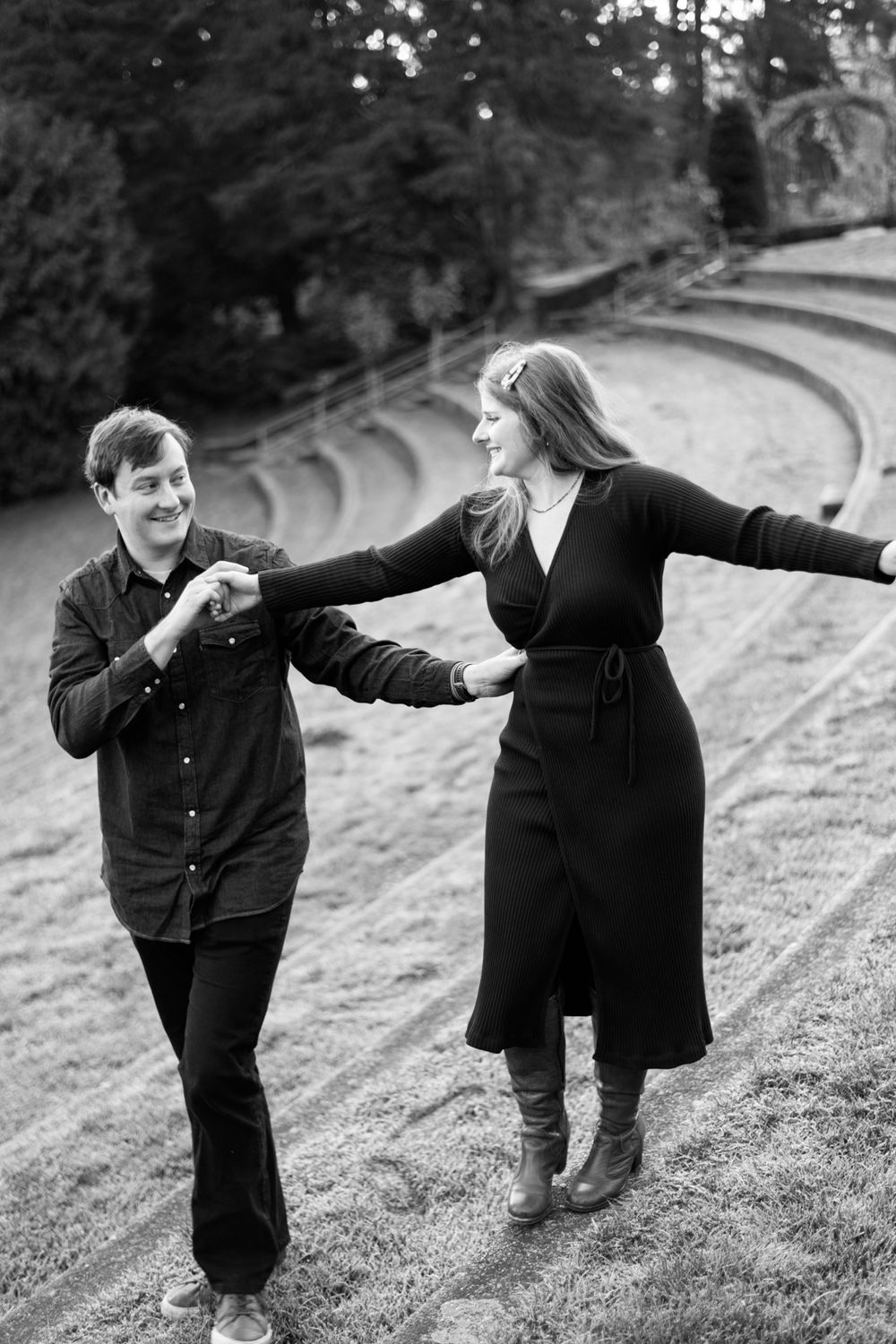 Black and white photo of two people dancing joyfully on a hillside amphitheater.