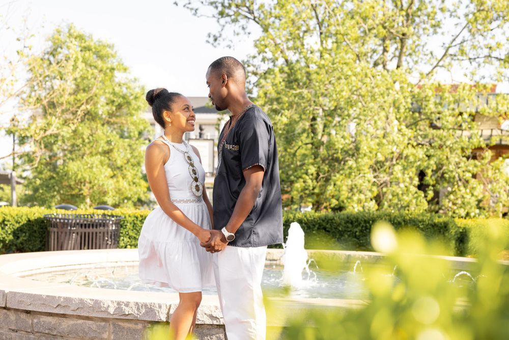 A couple shares a romantic moment in a sunlit park with lush greenery in the background.
