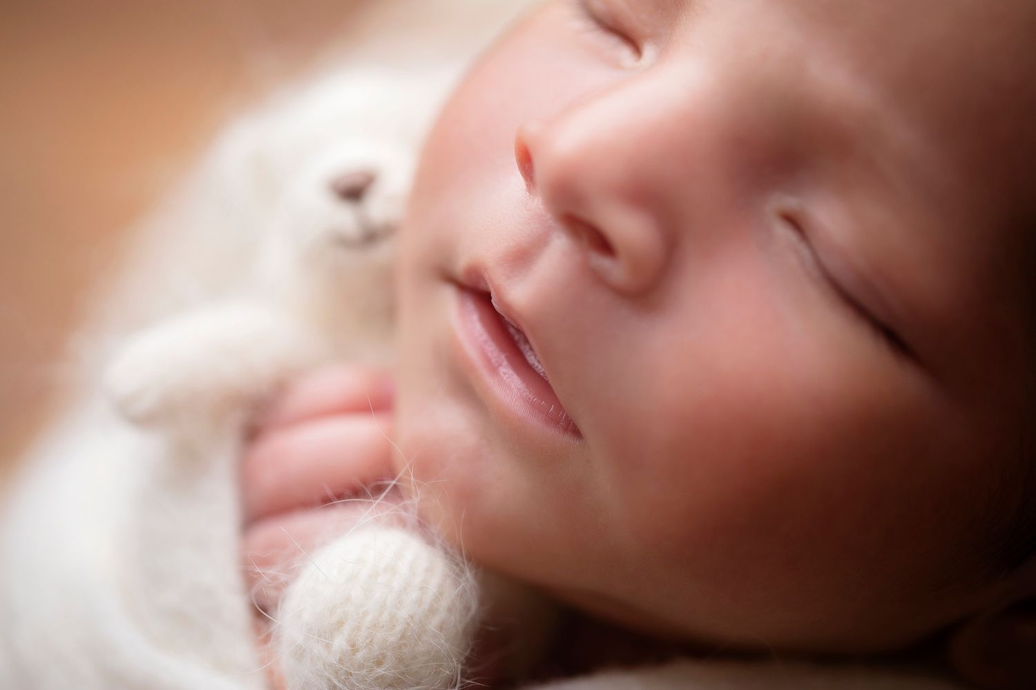 A peaceful sleeping newborn wrapped in soft white blanket with dreamy lighting.