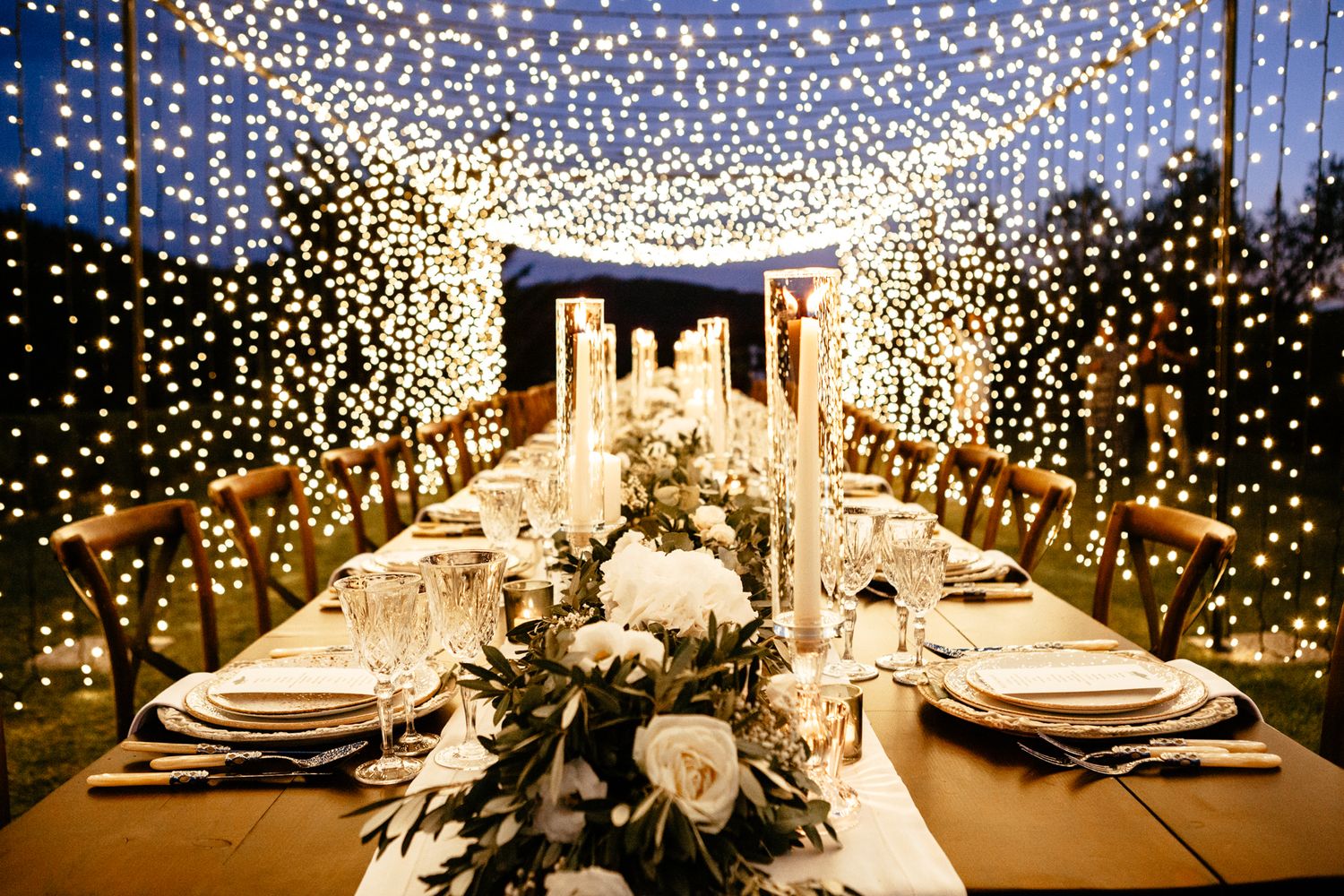 the table is set under a canopy of fairy lights for alfresco dinning at this Tuscan wedding