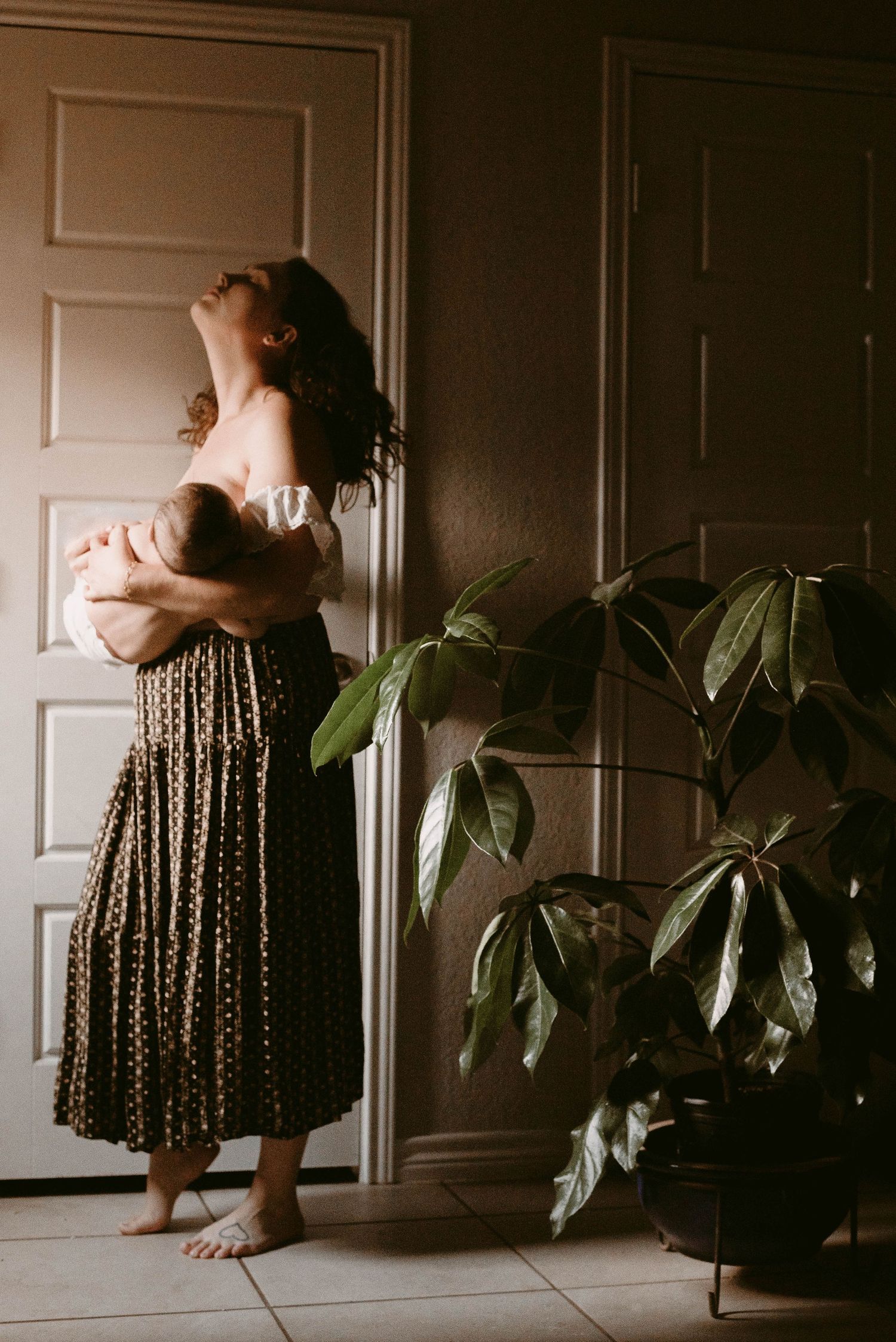 Artistic silhouette of woman and baby standing by door with large indoor plant.