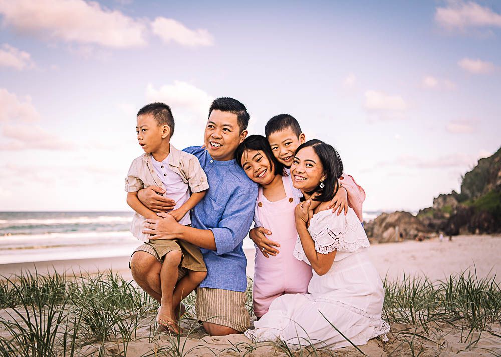 Family sharing joyful moments together while sitting on beach sand at sunset.