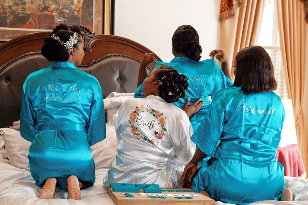 Group wearing matching turquoise robes sitting on bed during wedding preparations.