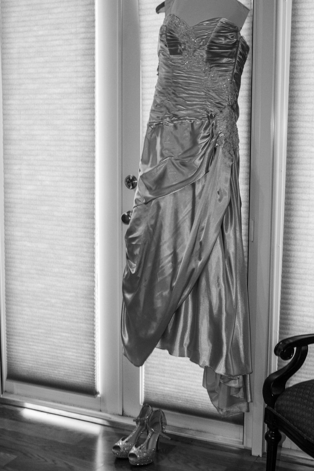 Elegant white wedding dress and heels hanging by window in black and white photography.