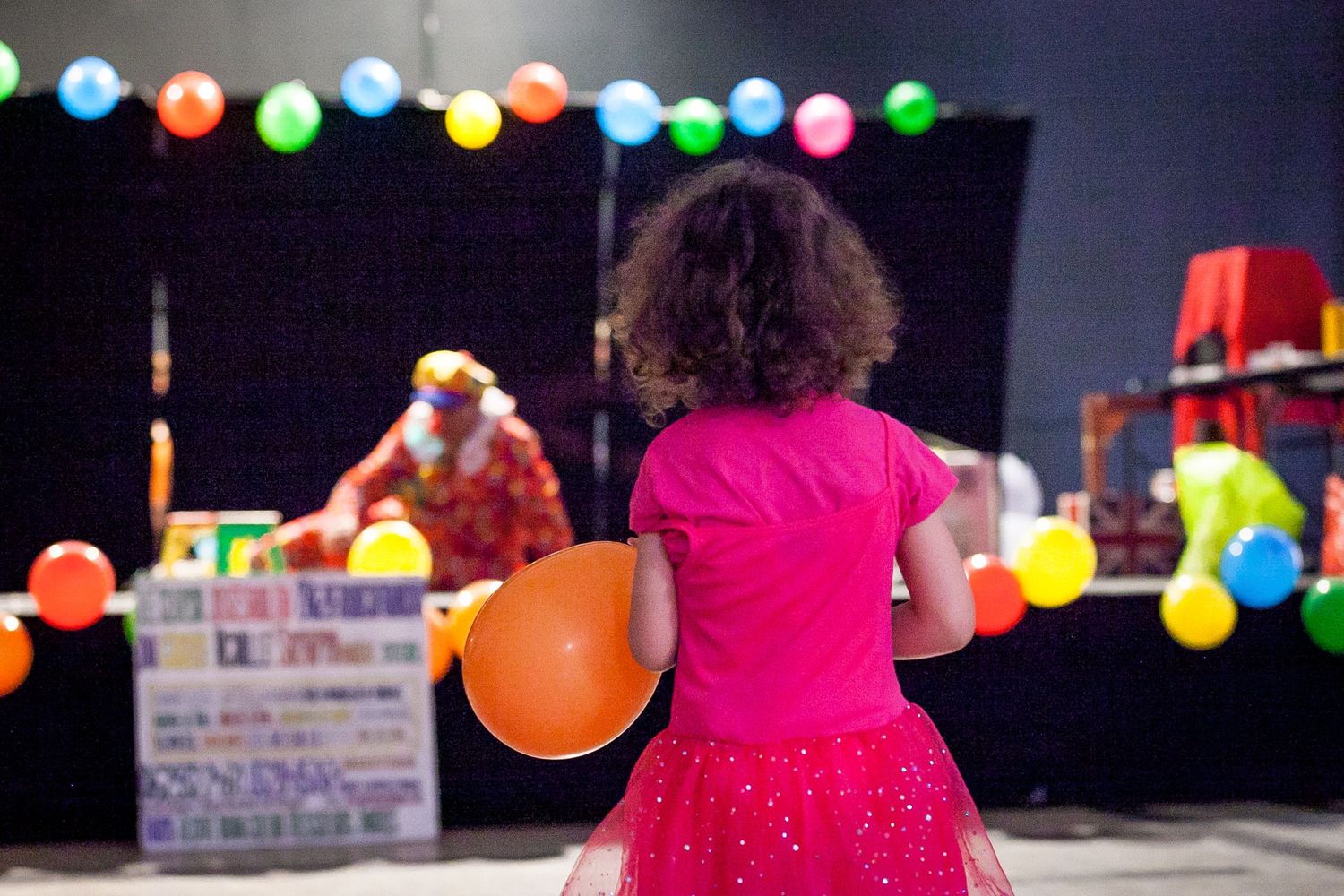 Fillette qui tient un ballon devant une scène avec un clown lors d'un évènement caritatif