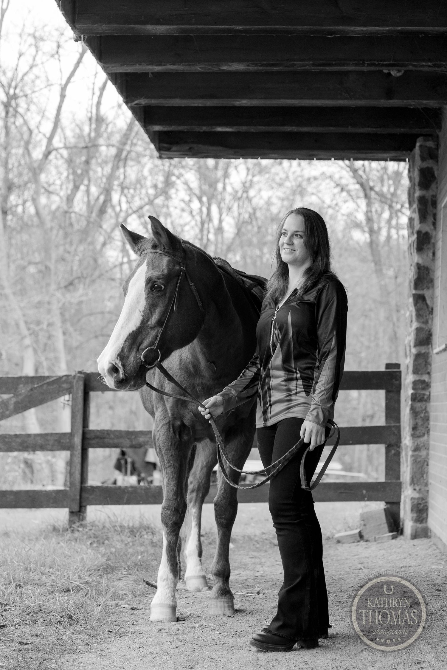 A monochrome image shows a horse and handler standing beneath a covered barn porch.
