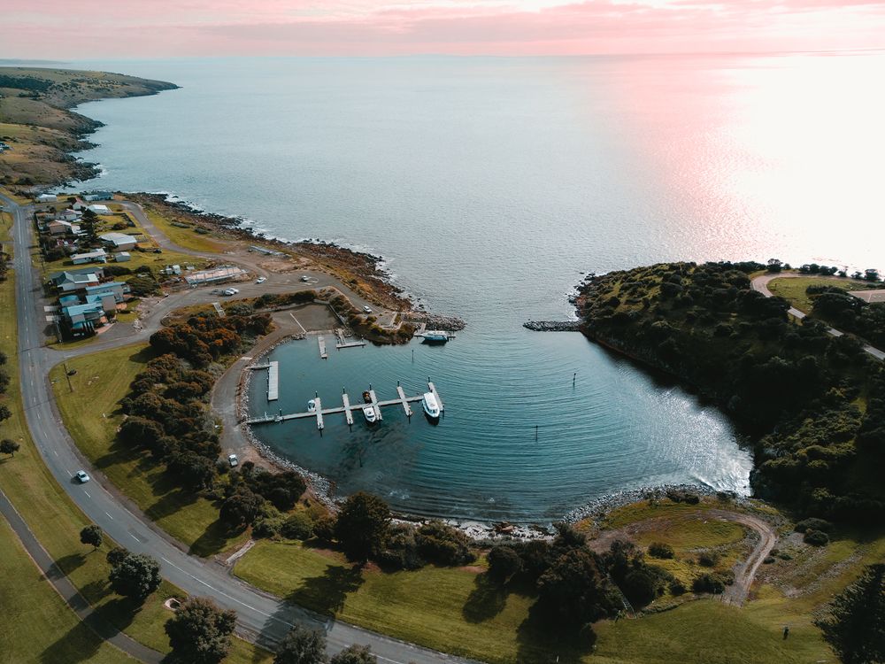Aerial view of a coastal marina with boats and winding road during sunset.
