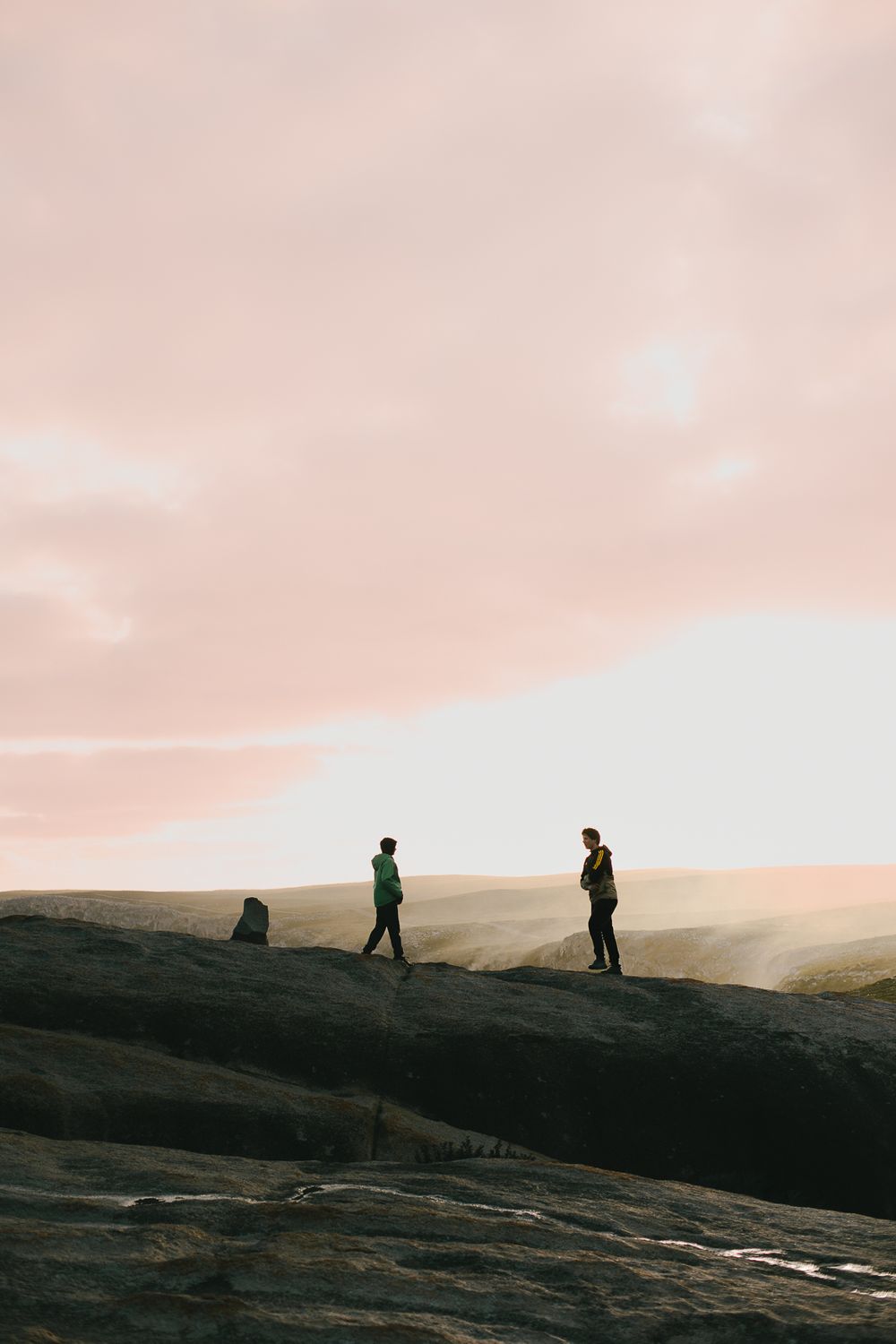 Silhouettes of people standing on rocky hill during sunset.