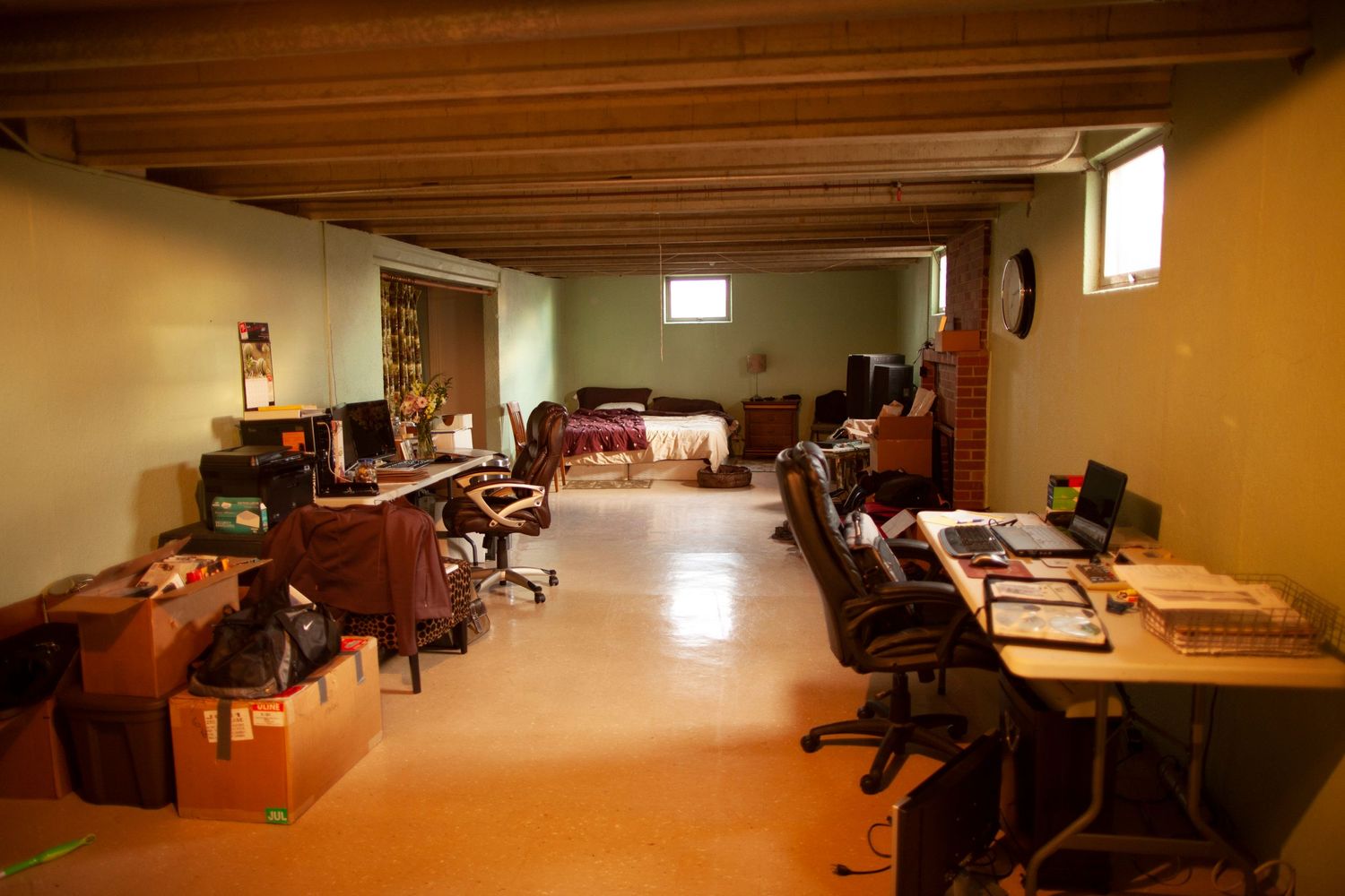Large basement room with wooden ceiling beams and scattered furniture.