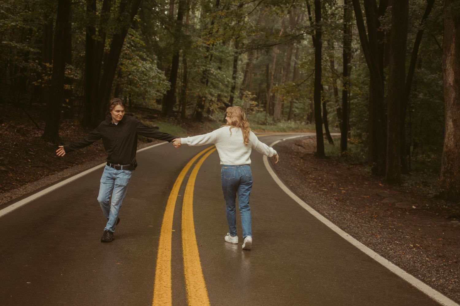 Playful couple running and jumping on a yellow lined road through a forest.