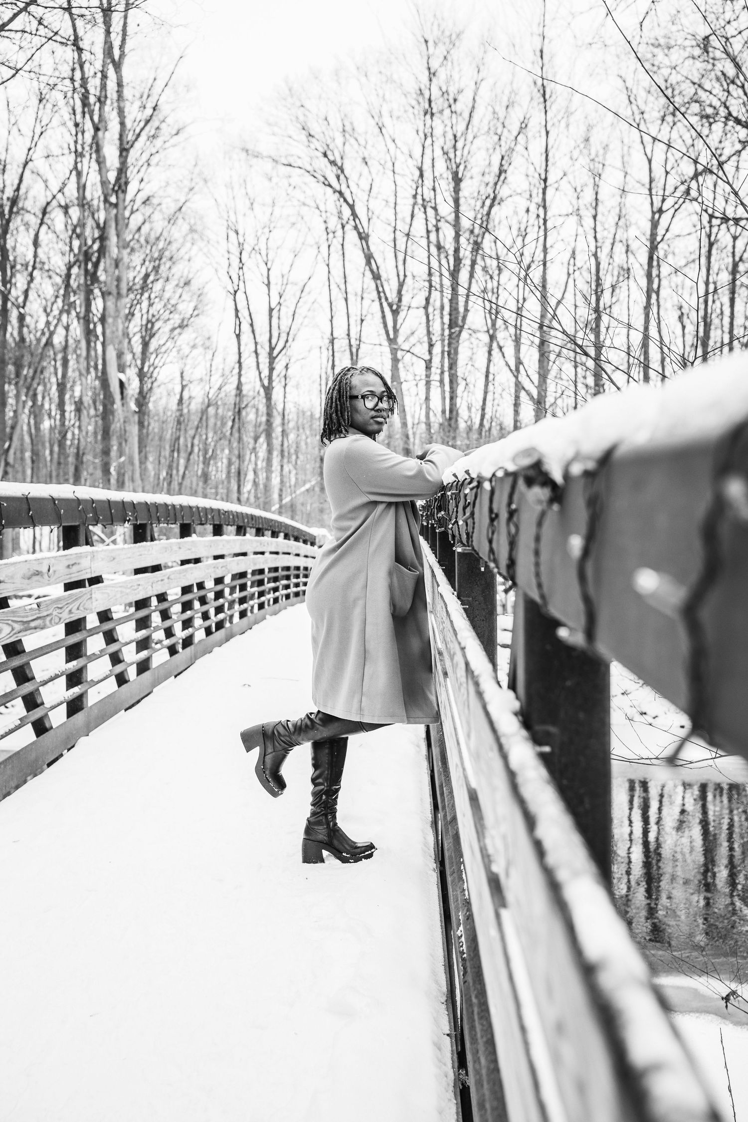 Black and white winter portrait on snow-covered bridge with coat and boots.