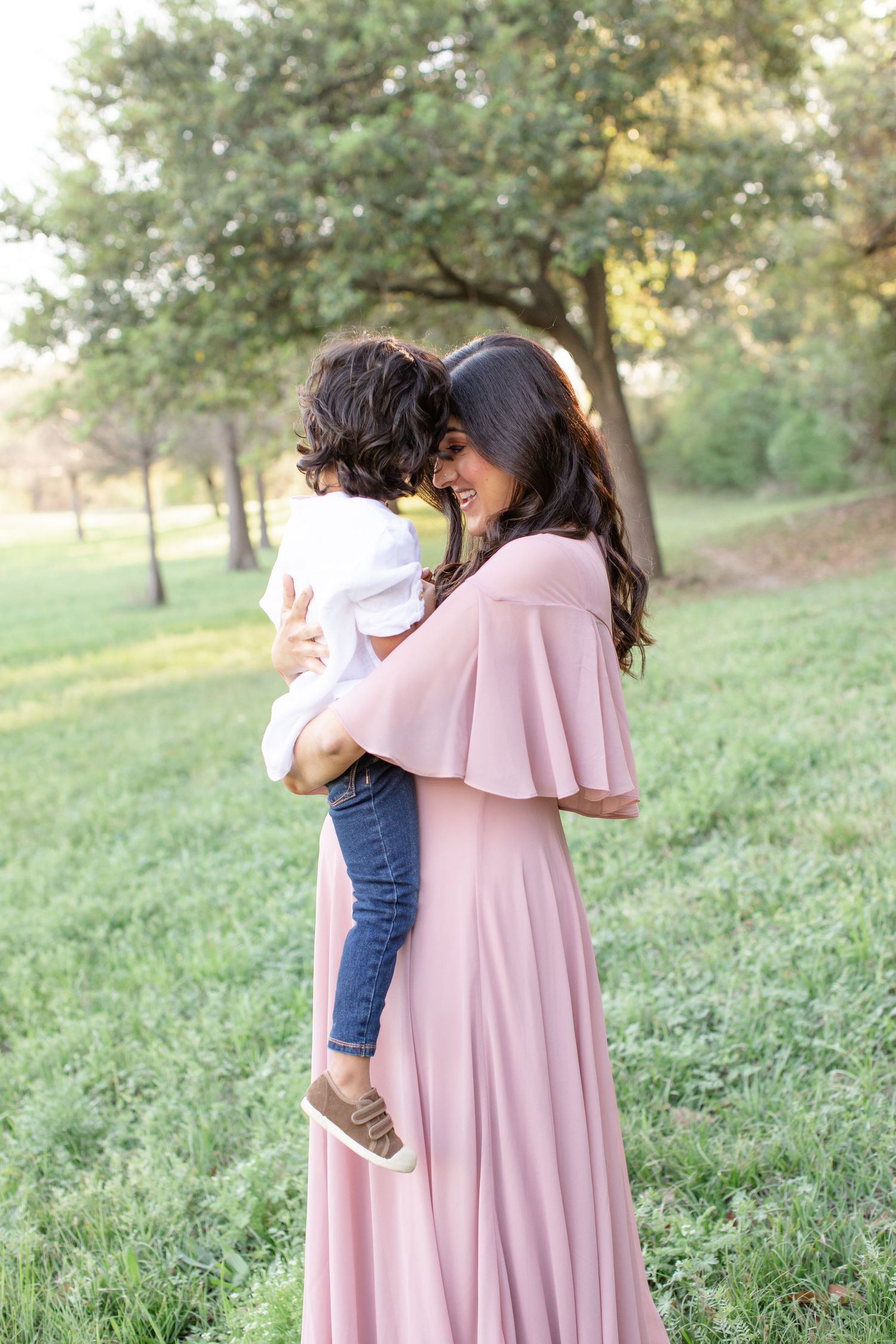A touching mother-child embrace captured in soft lighting with green park scenery.