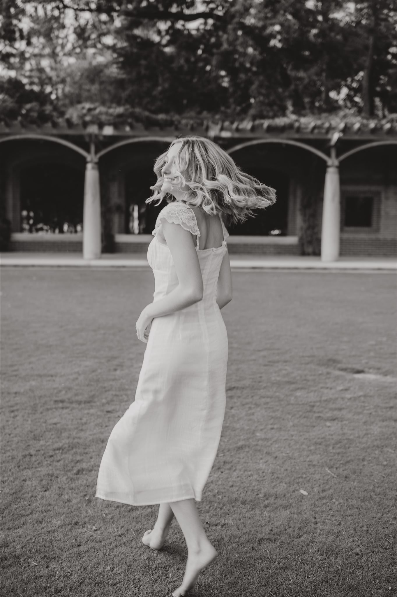 Black and white photo of spinning dance movement in flowing white dress outdoors.