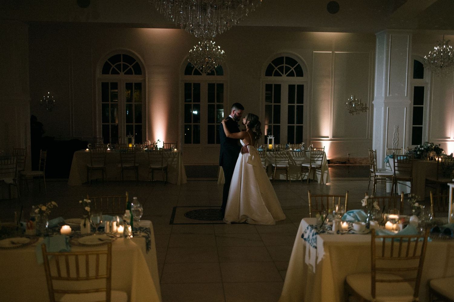 A romantic evening wedding reception scene with candlelit tables and a couple dancing in an elegant ballroom.