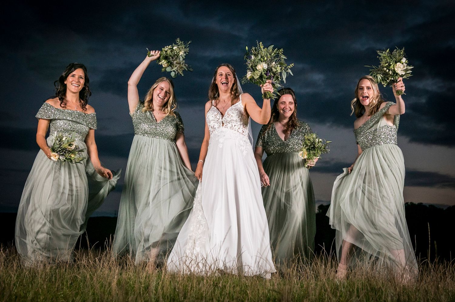 Wedding party poses dramatically at sunset with bridesmaids in sage green dresses.