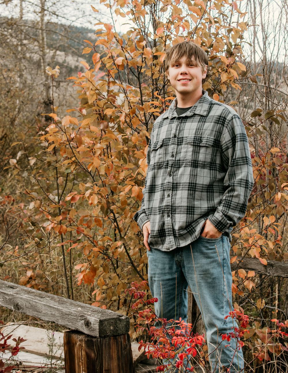 Person in plaid flannel shirt stands among autumn foliage on mountain trail.