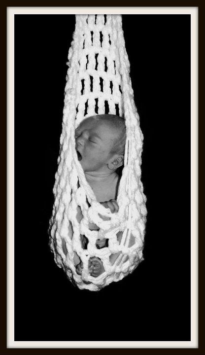 Black and white image of sleeping newborn in macrame hanging basket.
