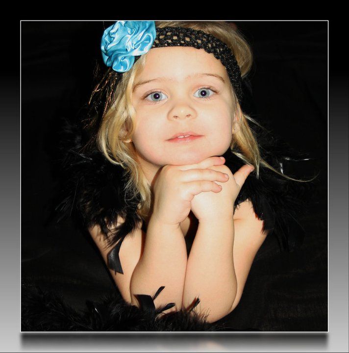 Portrait of child with blue flower headband against dark background.