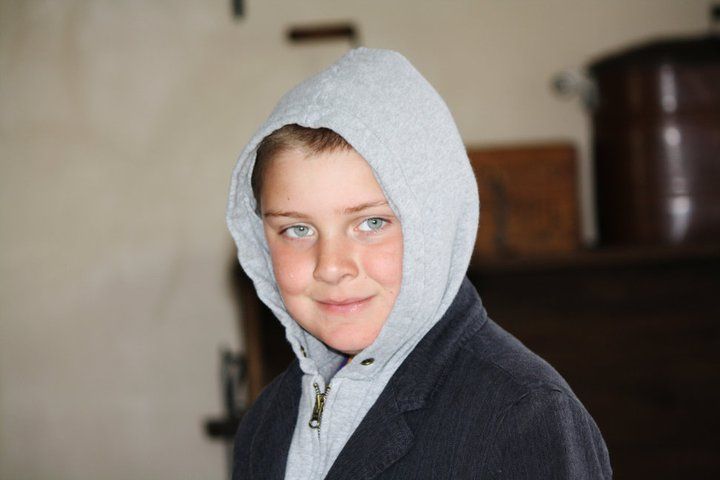 Young person wearing a light gray hooded sweatshirt and dark jacket looking at camera.