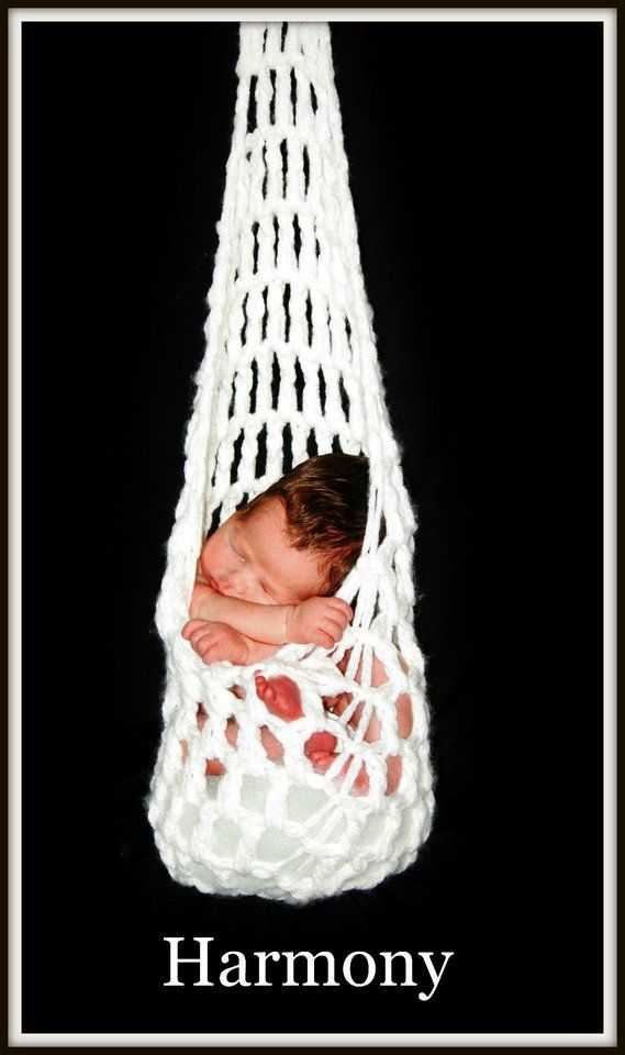 Artistic newborn photography featuring white macrame hanging cradle against black background.