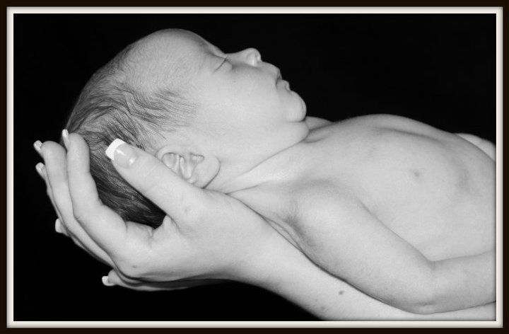 Black and white photo of newborn baby cradled in hands.