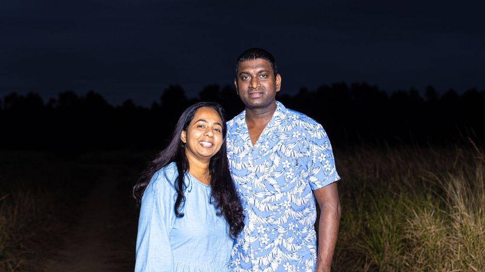 Couple in matching blue and white outfits pose together in a field at dusk.