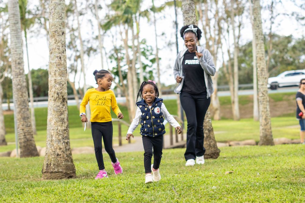 A family enjoys a sunny day walking together in a park with tall trees.
